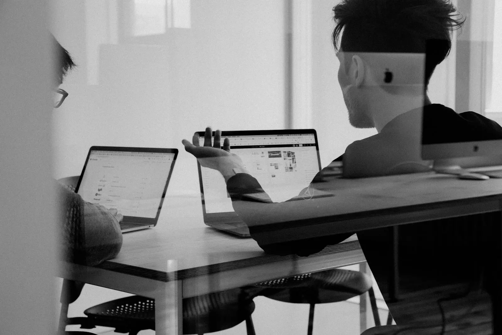 Two engineers reviewing a build at their laptops, monochrome reflection across the workspace.